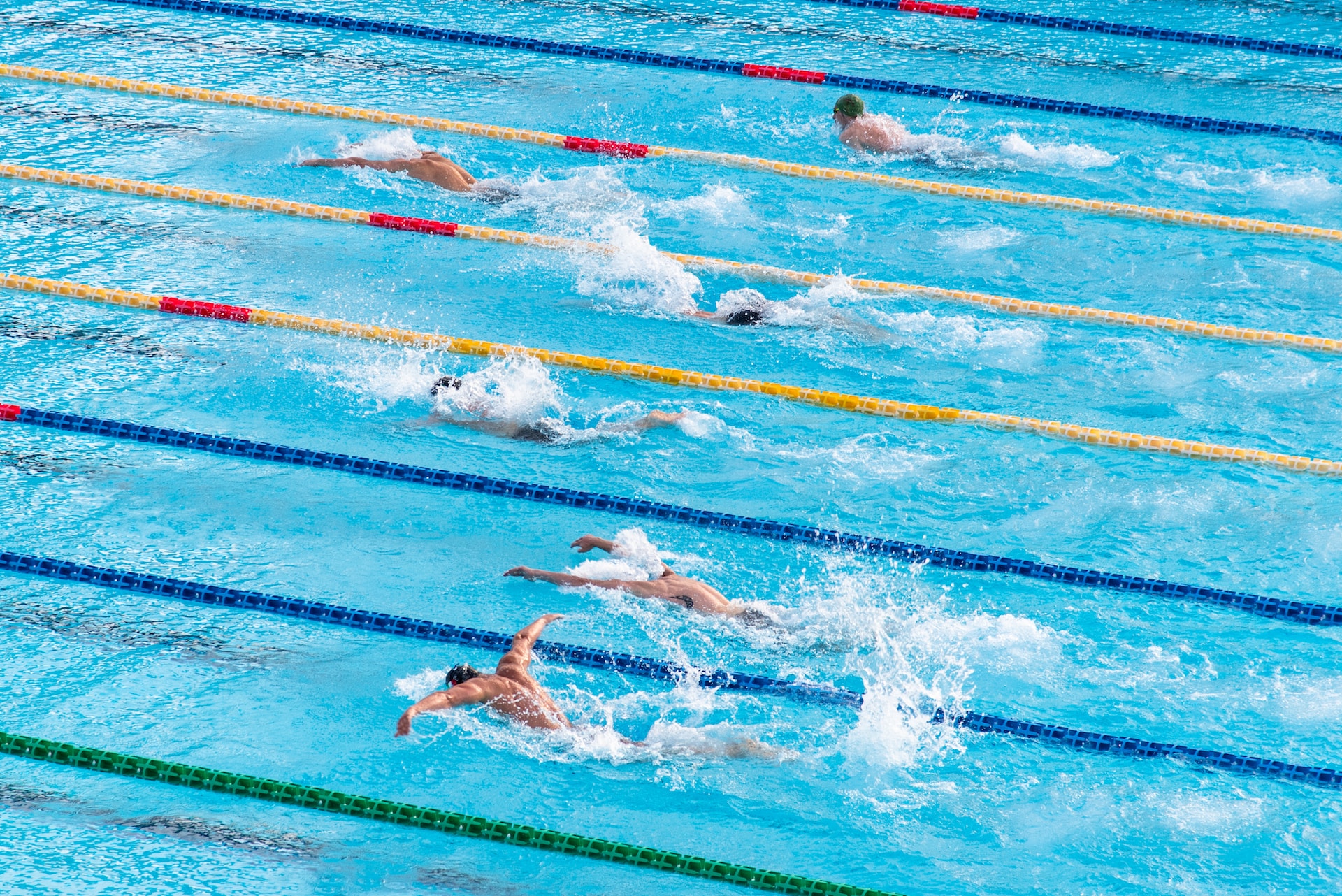 Six swimmers in a swimming pool, competing in a race. One swimmer is leading by quite some way.